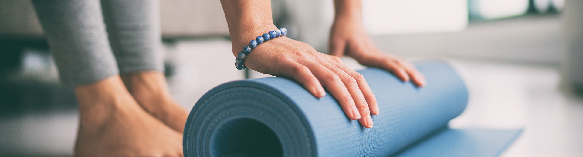 Nahaufnahme: Hände rollen Yogamatte aus, barfuß mit grauer Leggings