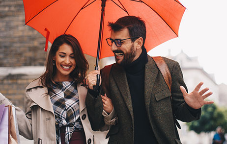 Mann mit orangen Regenschirm läuft mit eine jungen hübschen Frau in der Stadt