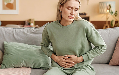 Frau sitzt auf einem Sofa und hält sich mit beiden Händen den Bauch.