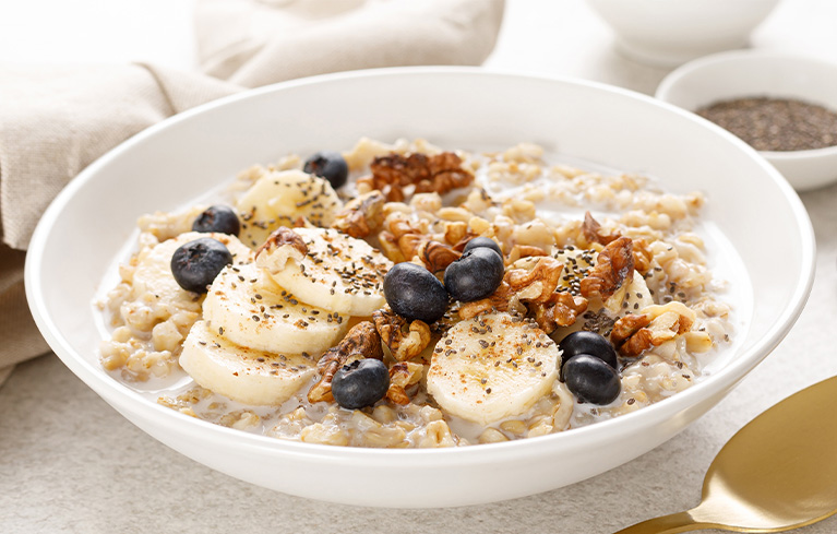 Schüssel mit Porridge, belegt mit Bananenscheiben, Blaubeeren, Walnüssen und Chiasamen.
