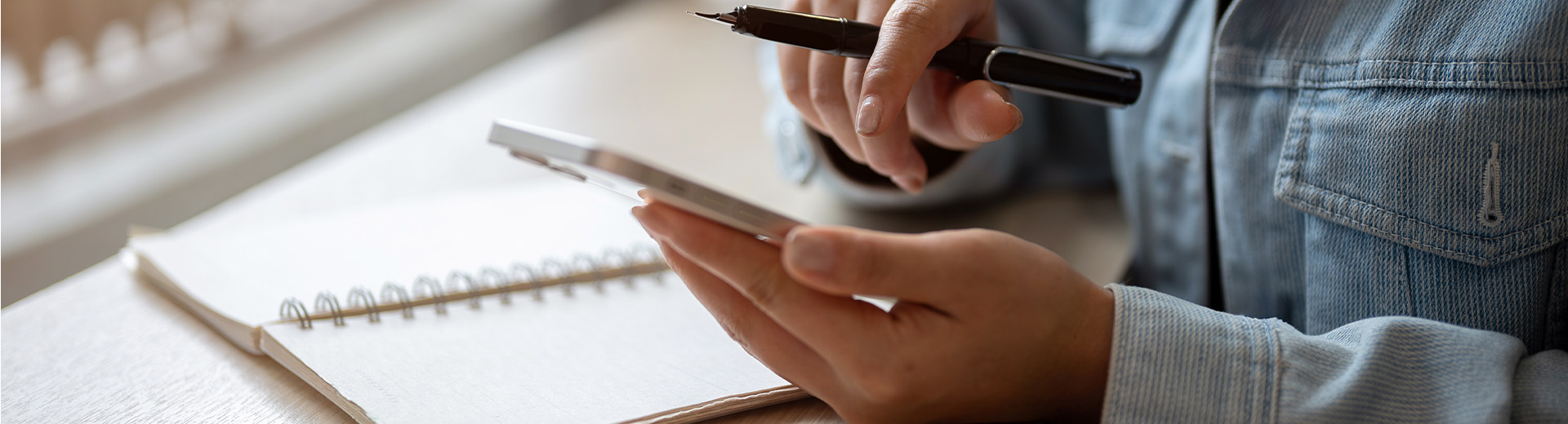 Frau mit Stift in der Hand schaut etwas auf ihrem Handy nach