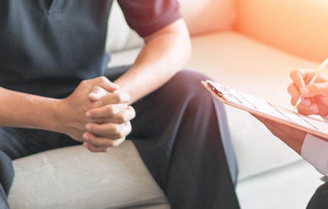 Junger Mann, Hände gefaltet, und Arzt im Gespräch