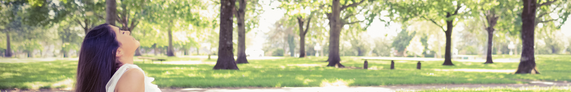 Entspannte Frau im Park auf grüner Wiese unter Bäumen