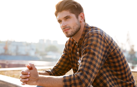 Junger Mann schaut nachdenklich, auf seine Arme gestützt