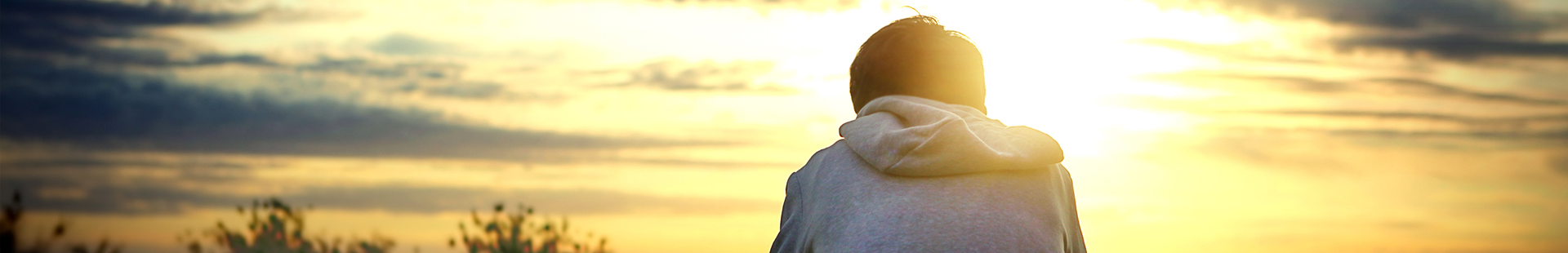 Frau sitzt abgewendet im Abendlicht, den Himmel anschauend
