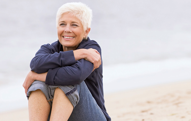Frau sitzt zufrieden lächelnd am Strand