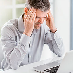 Mann, am Computer sitzend und die Hände am Kopf haltend