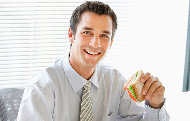 Mann isst während der Arbeit im Büro ein belegtes Brötchen