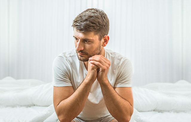 Mann sitzt nachdenklich und betrübt auf der Bettkante