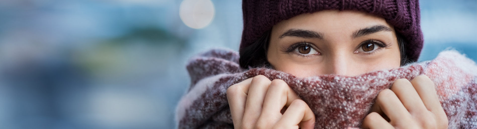 Junge Frau mit Schal und Mütze, hebt glücklich Schal über Nase