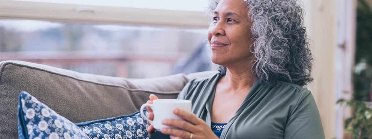Ältere Frau schaut entspannt und glücklich mit einer Tasse Tee aus dem Fenster