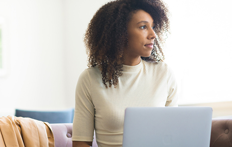 Junge Frau sitzt nachdenklich schauend vor dem Laptop
