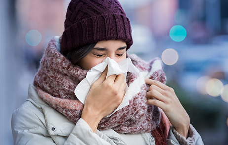 Sich schnäutzende junge Frau, winterlich gekleidet auf der Straße