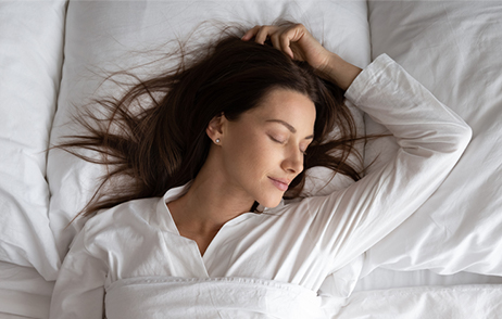 auf dem Rücken schlafende junge Frau, ein Arm angewinkelt über dem Kopf, entspannter Gesichtsausdruck