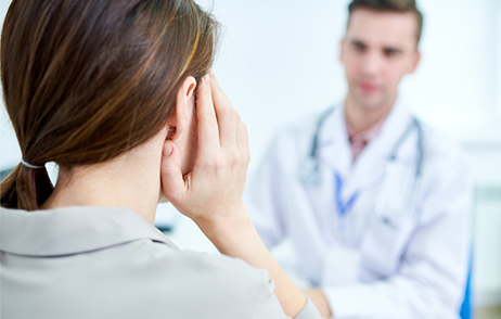 Frau fasst sich ans Ohr, Gespräch mit Arzt