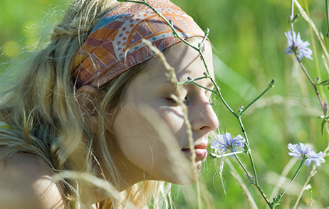 Frau riecht an Blume, auf Wiese liegend