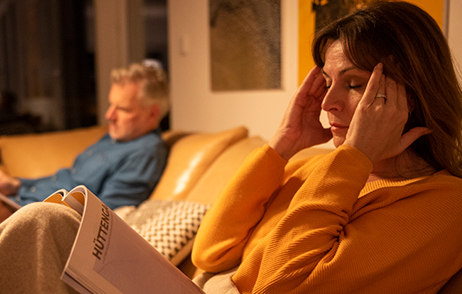 Frau mit Kopfschmerzen auf dem Sofa sitzend, abendliche Stimmung