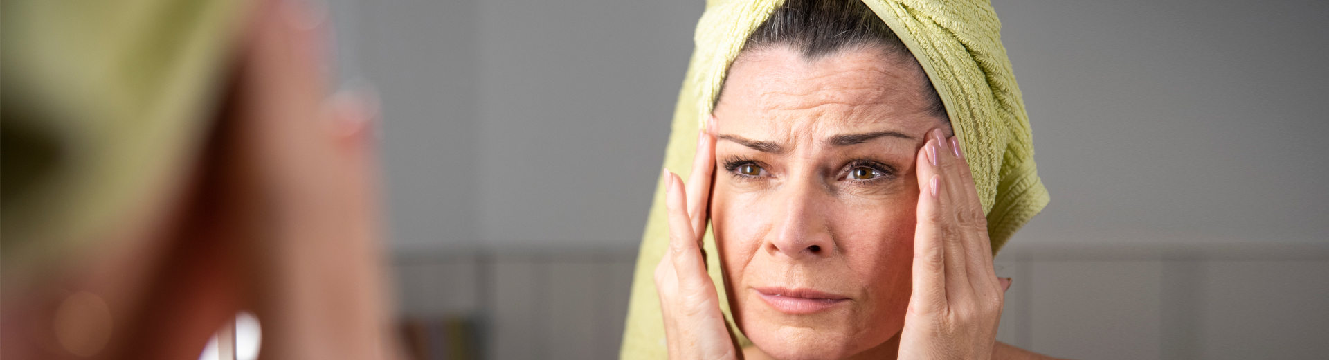 Frau mit kritischem Blick vor Spiegel, Hand an der Schläfe