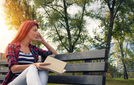 Junge Frau sitzt auf einer Parkbank und schaut nachdenklich in die Ferne