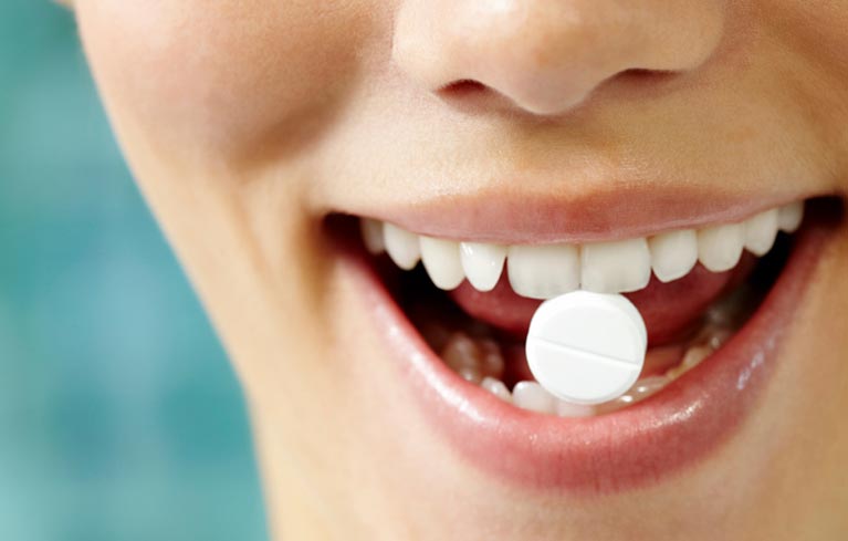 Frau hält eine Tablette zwische den Zähnen