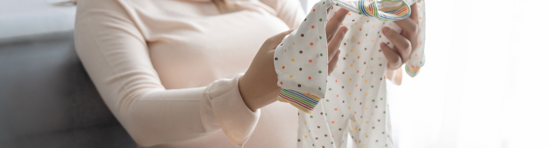 Schwangere Frau betrachtet Strampelanzug