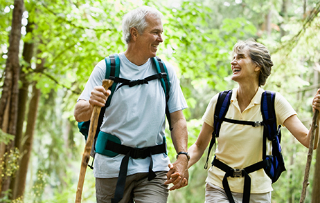 Lächelndes Wanderpaar mit Rucksäcken auf Waldweg bei Sonnenschein