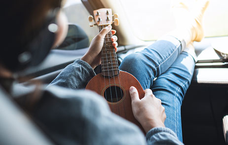 Frau sitzt entspannt im Auto und spielt eine kleine Gitarre