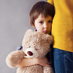 Traurig schauendes Kind mit Teddy im Arm schmiegt sich an seine Mutter