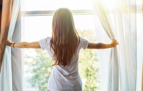 Frau macht morgend die Vorhänge auf