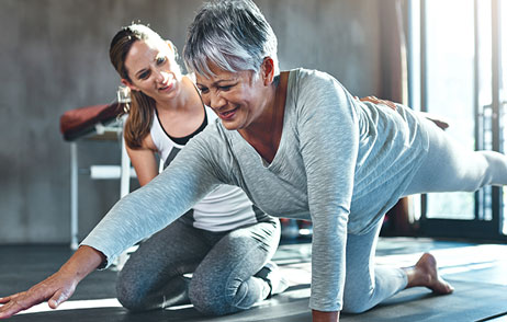 ältere Frau macht Rückenübungen mit einer Betreuung