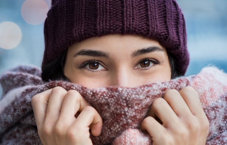 Junge Frau mit Mütze und Schal vor dem Mund