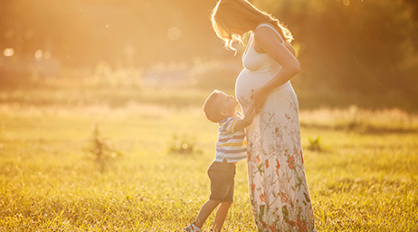 Schwangere mit Kleinkind stehend auf Wiese, Kind schaut zu Mama hoch