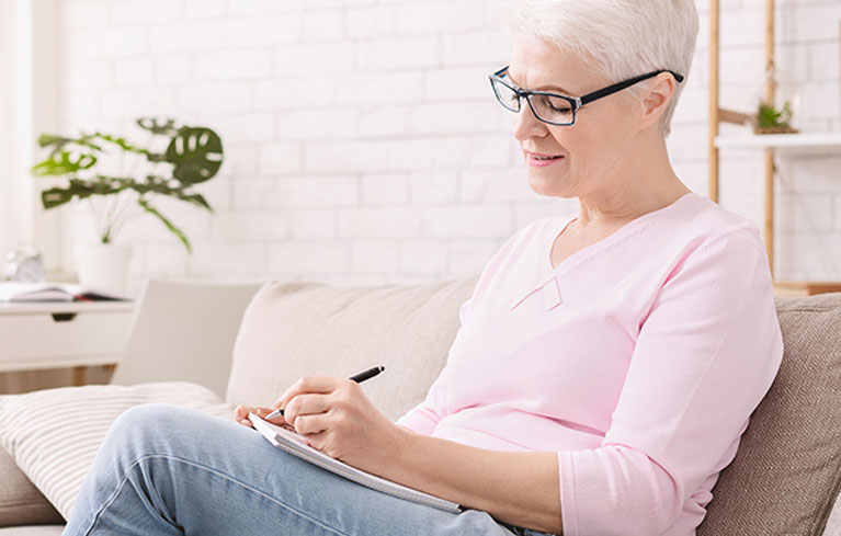 ältere Frau sitzt zu Hause und notiert sich etwas 