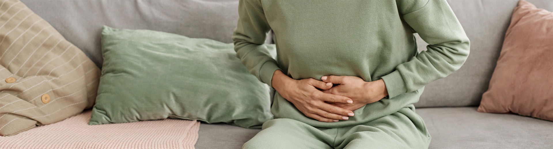 Frau hält sich mit beiden Händen den Bauch auf Sofa sitzend