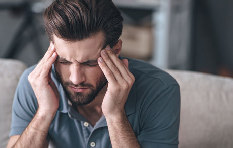 Junger Mann auf dem Sofa mit Kopfschmerzen