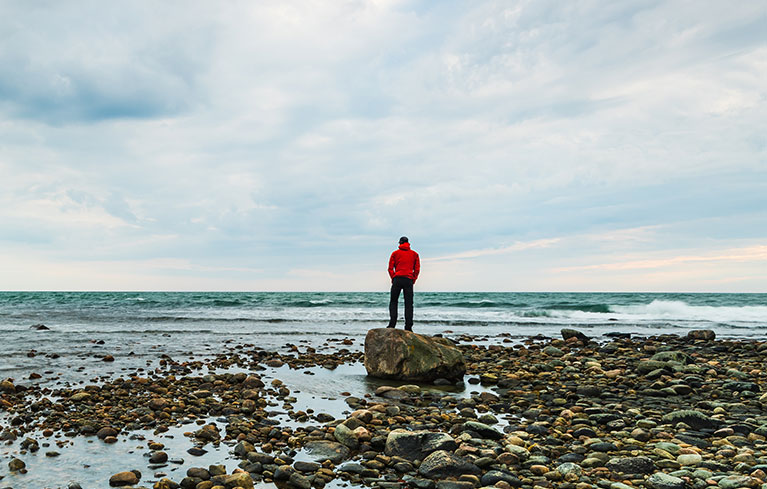 Mann am Steinstrand schaut auf das Meer
