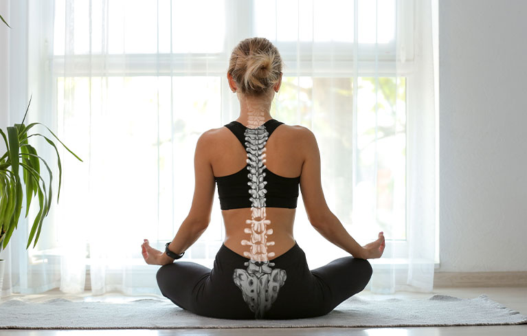 Frau sitzt im Schneidersitz vor einem hellen, großen Fenster