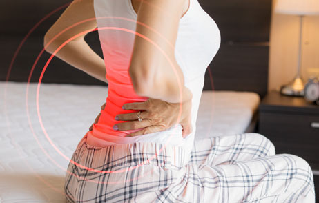 Frau sitzt auf Bettkante und hebt sich am Rücken