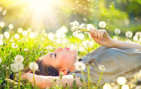 Frau im Gras liegend mit Pusteblumen