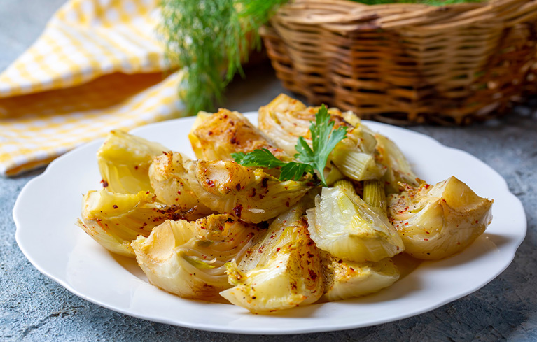 Geschnittenes Fenchelgemüse auf einem weißen Teller mit einem grünen Kräuterblatt.