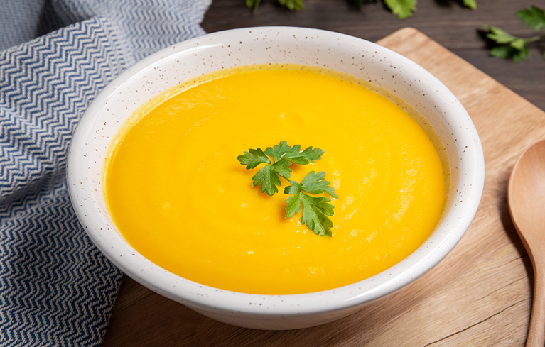Schüssel mit gelber Cremesuppe, garniert mit zwei Petersilienblättern.