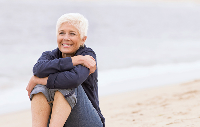 Frau sitzt zufrieden lächelnd am Strand