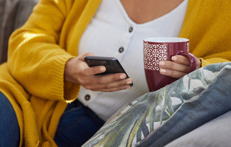 Frau mit Handy in einer und Tasse tee in der anderen Hand