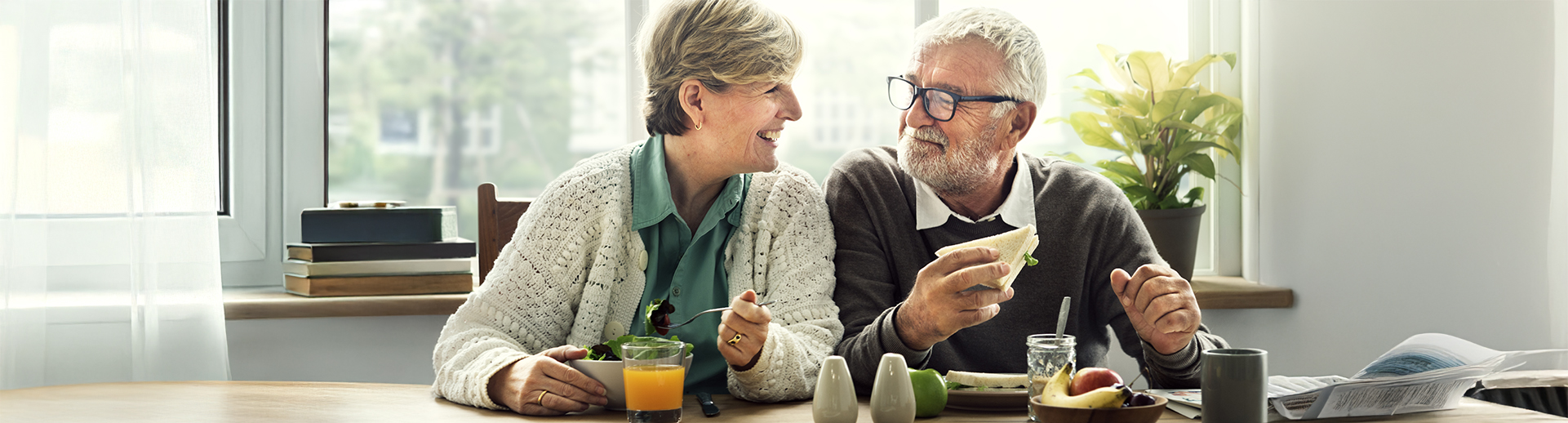 Zwei ältere Personen sitzen gemeinsam am Tisch, essen und lächeln sich an