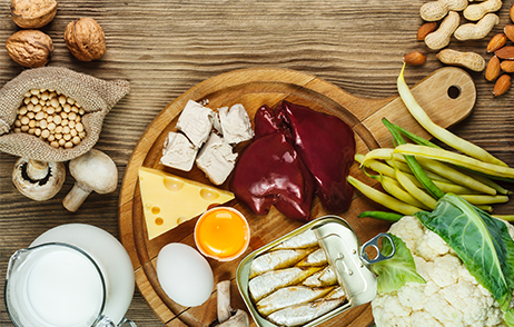 Verschiedene Lebensmittel wie Fisch, Milchprodukte, Gemüse, Nüsse und Hülsenfrüchte liegen auf einer Holzfläche