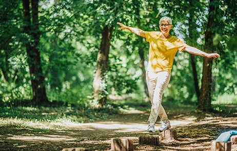 Person balanciert auf Holzstämmen im Wald bei Sonnenlicht