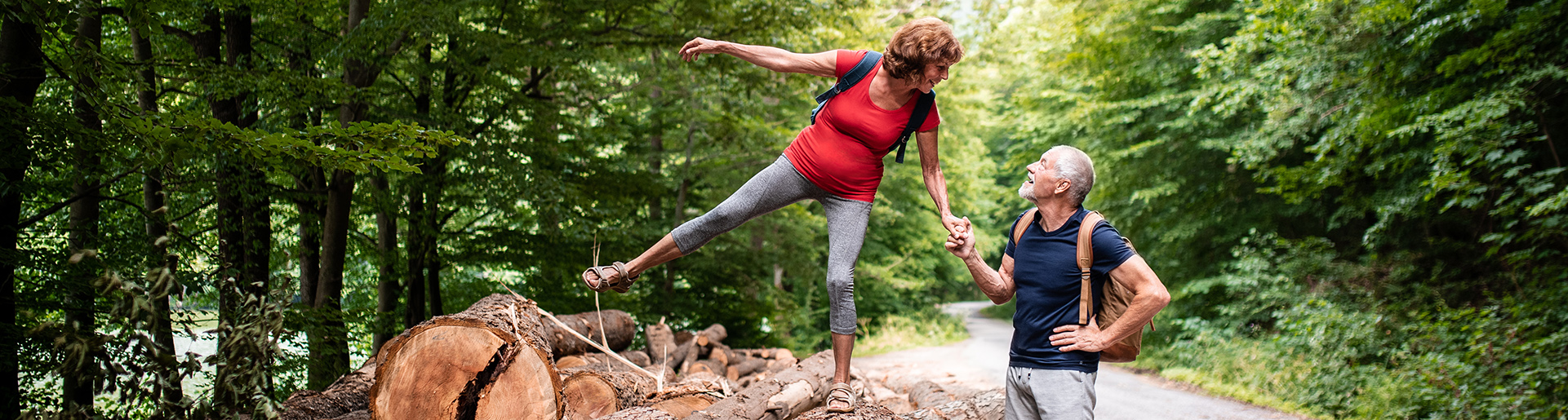 Zwei Erwachsene beim Wandern im Wald, einer balanciert auf Baumstämmen